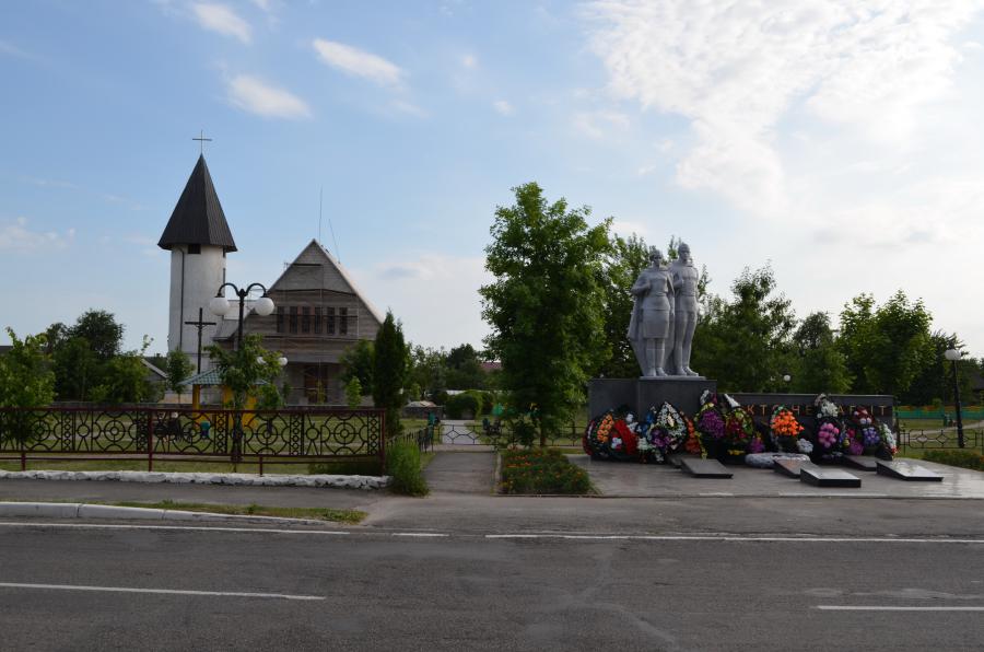 Лельчицкий парк. За ним виден костел, а на переднем плане памятник воинам погибшим в ВОВ.